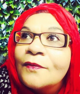 A woman with rectangular glasses and a red headscarf looks up and to the side