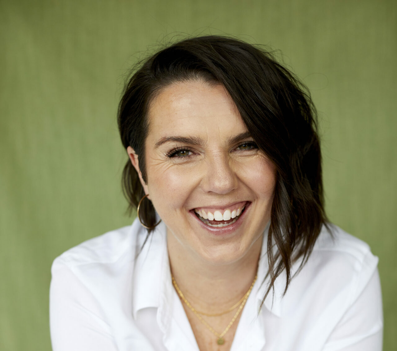 A photograph of a laughing white woman with shoulder length straight dark hair and a white blouse
