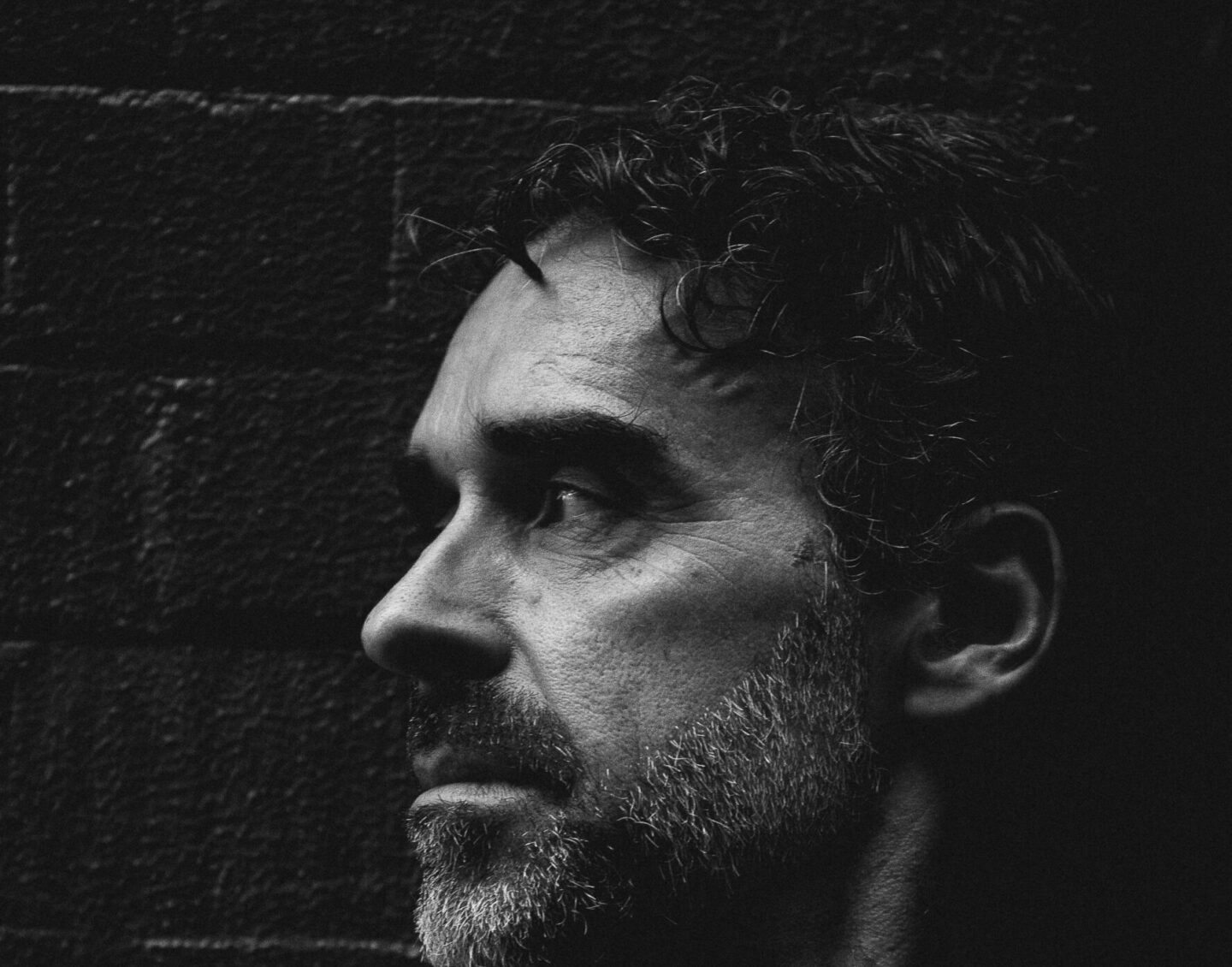 A black and white photo of a man in side profile with dark curly hair and a short beard