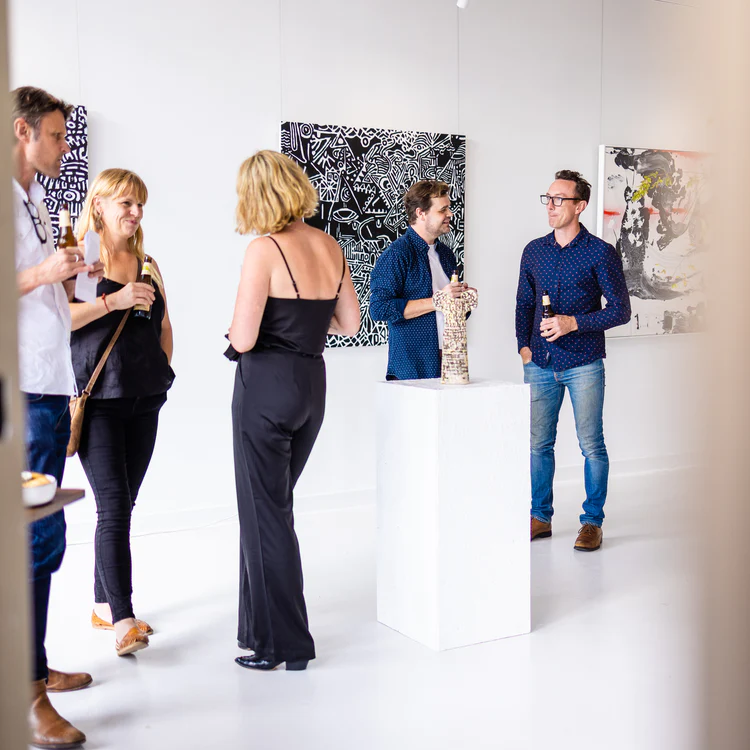A group of people stand, drinks in hand, talking to each other in an art gallery