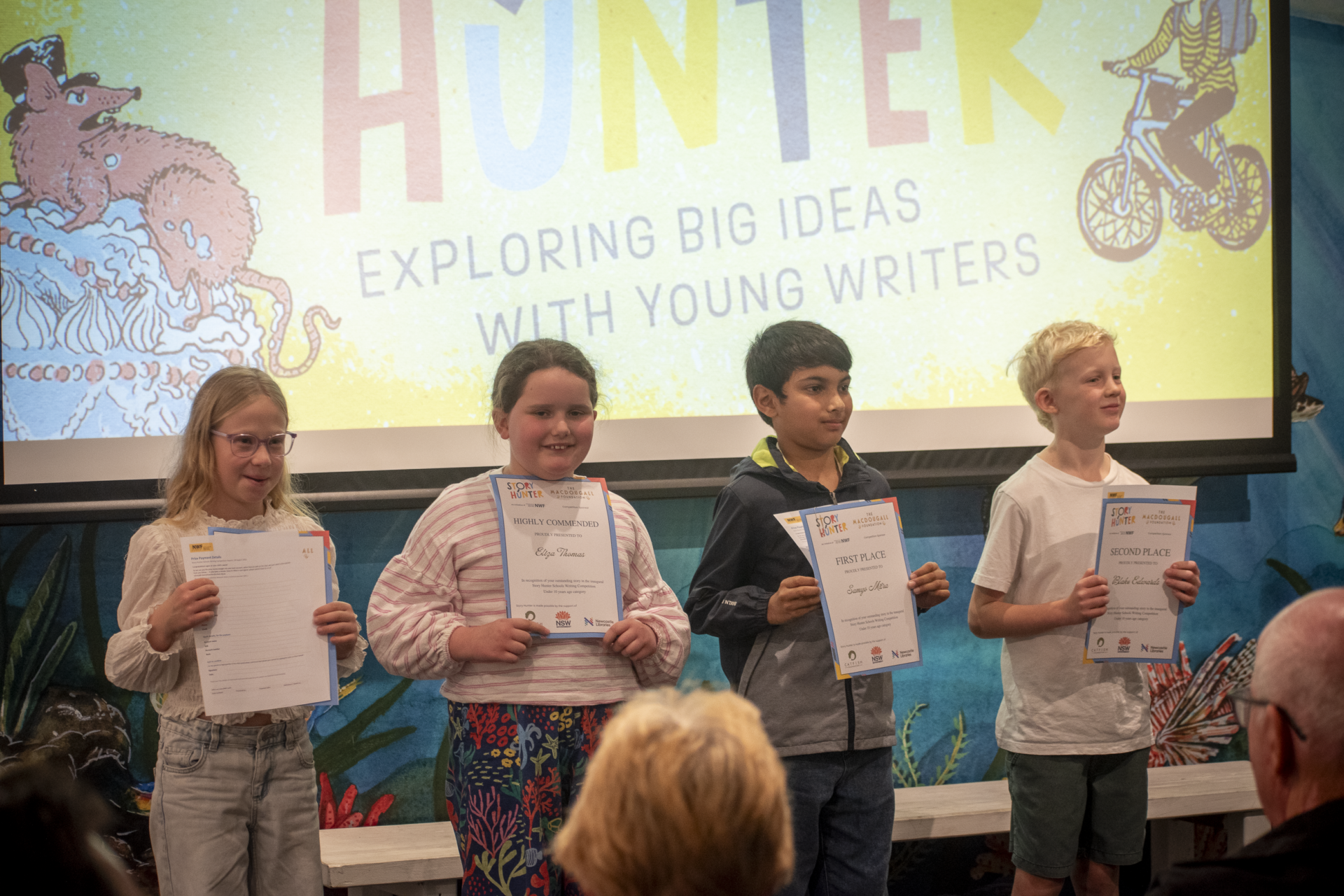 From left to right Brönte Edwards, Eliza Thomas, Samyo Mitra, and Blake Edwards are shown holding their certificates of achievement in front of a digital Story Hunter banner. From left to right Brönte Edwards, Eliza Thomas, Samyo Mitra, and Blake Edwards are shown holding their certificates of achievement in front of a digital Story Hunter banner.