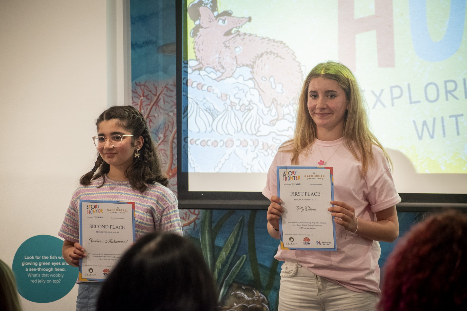 From left to right, Zarleena Muhammad and Tilly Diana are shown holding their certificates of achievement in front of a digital Story Hunter banner. From left to right, Zarleena Muhammad and Tilly Diana are shown holding their certificates of achievement in front of a digital Story Hunter banner.